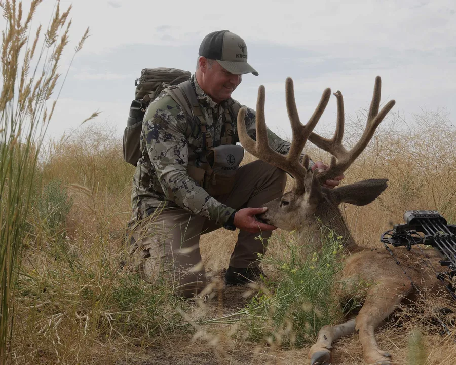 Hunter wearing Kings Camo in open country beside a mule deer